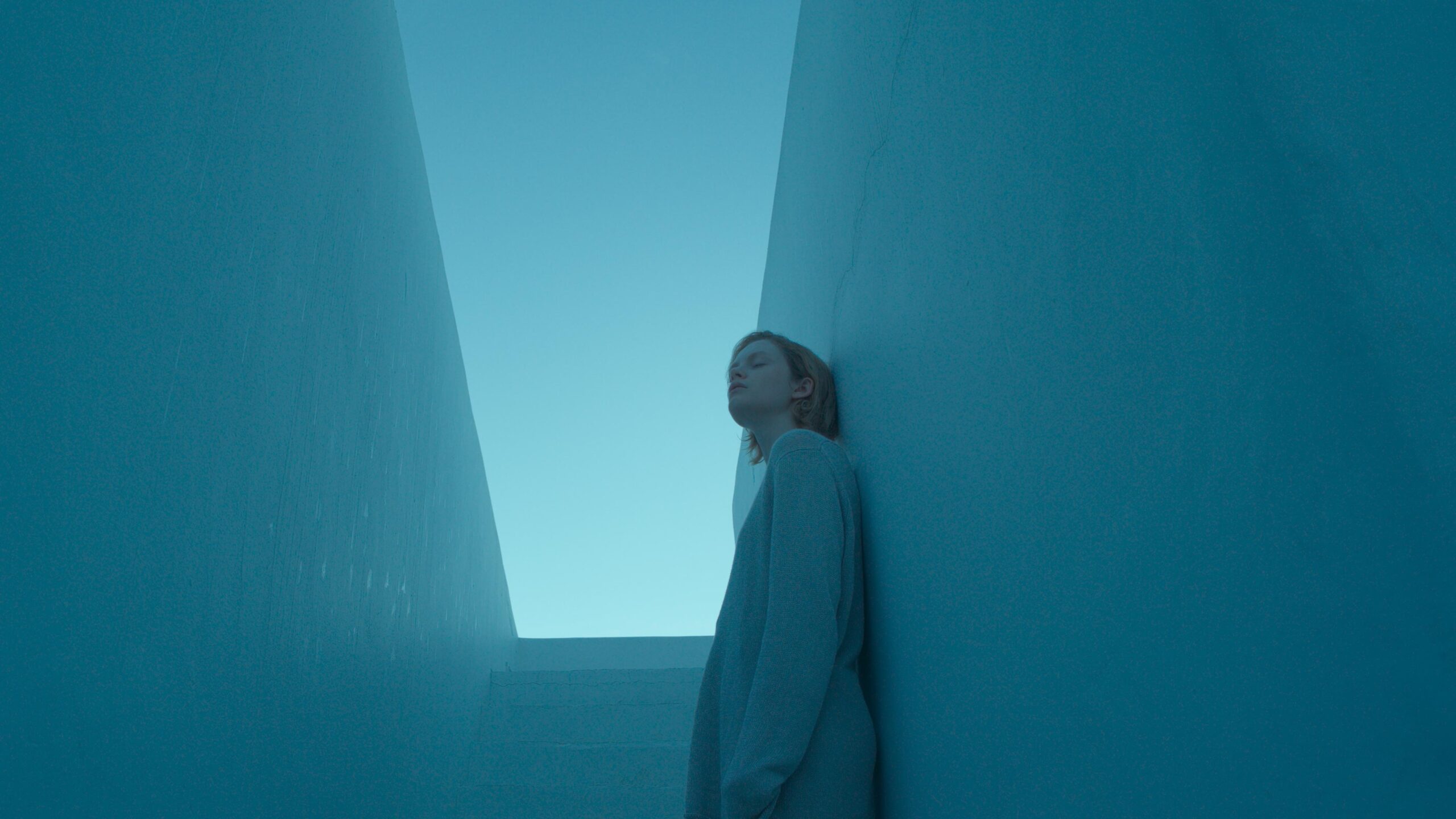 Emma Laird as Lola in the film Satisfaction, covered in blue with a sliver of light