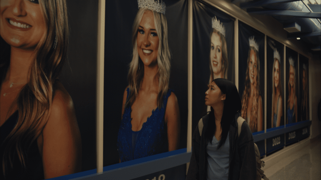 Shirley Chen looking at images of prom queens on the wall in the movie Slanted