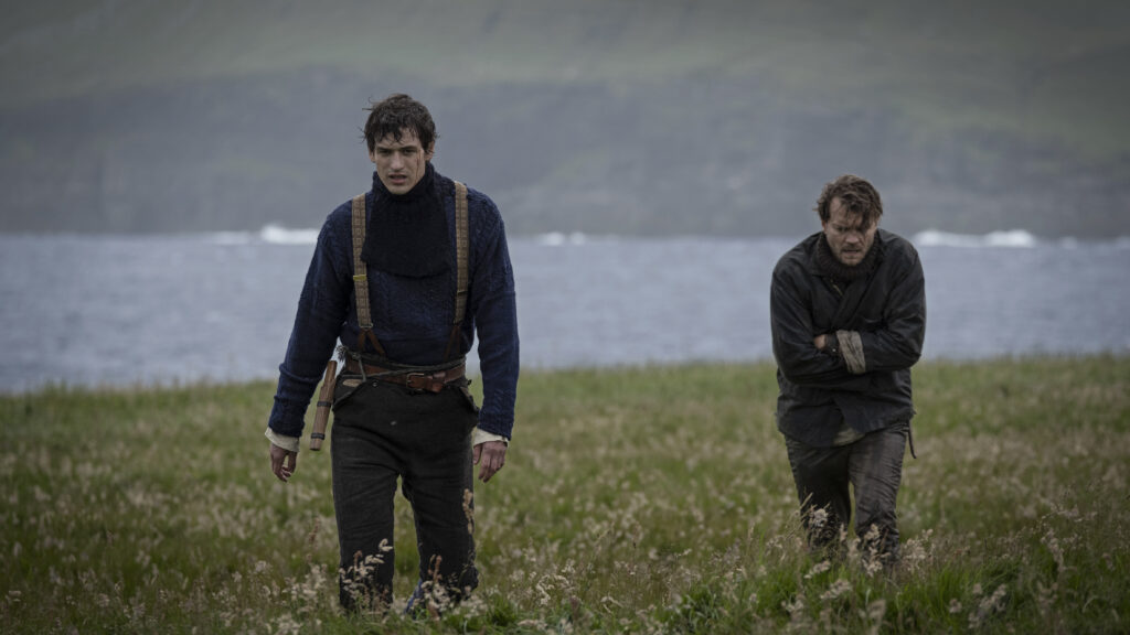 Egor Venned as Baldur and Pilou Asbæk as Helge cross a windswept coastal field in No Rest for the Wicked