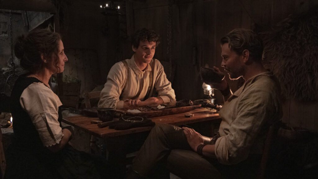 Sofia Nolsøe as Ásla, Egor Venned as Baldur, and Pilou Asbæk as Helge sit around a candlelit table in No Rest for the Wicked