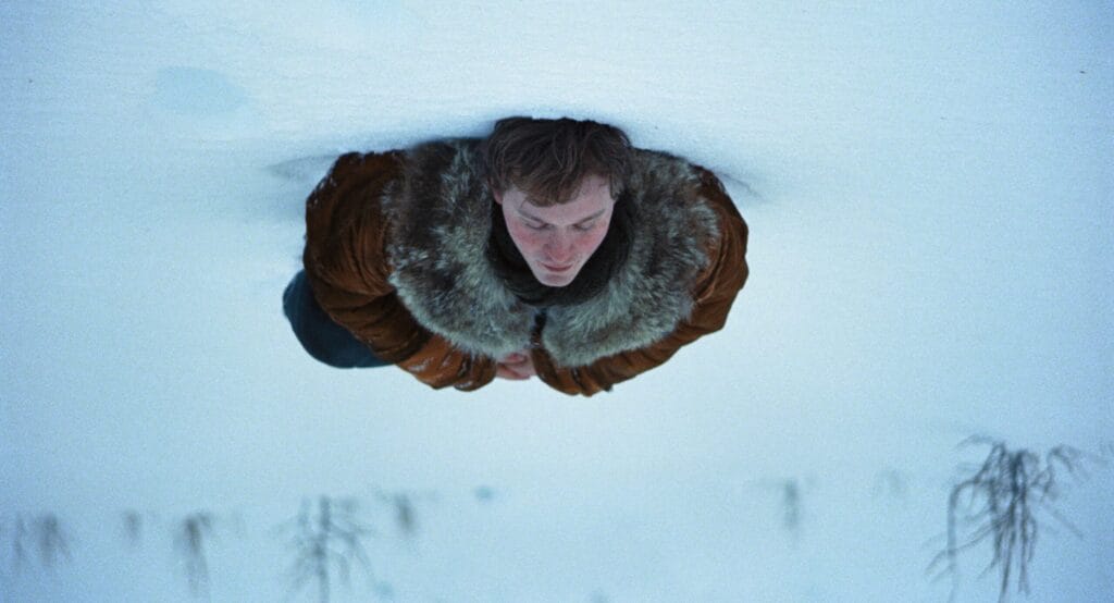 Young man in a fur-lined winter coat stands alone in deep snow in A Long Winter
