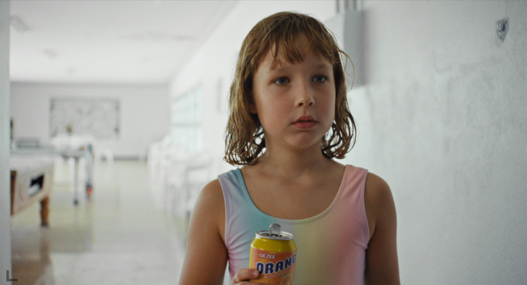 A young girl with wet hair holds a can of orange soda in a bright white hallway in Everytime.