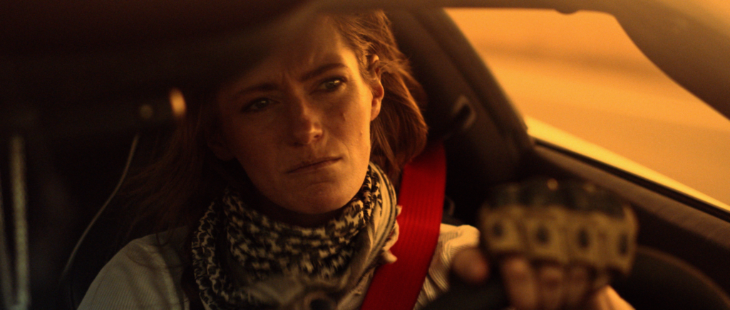 Woman sits inside a car under warm orange light in X-Communicado